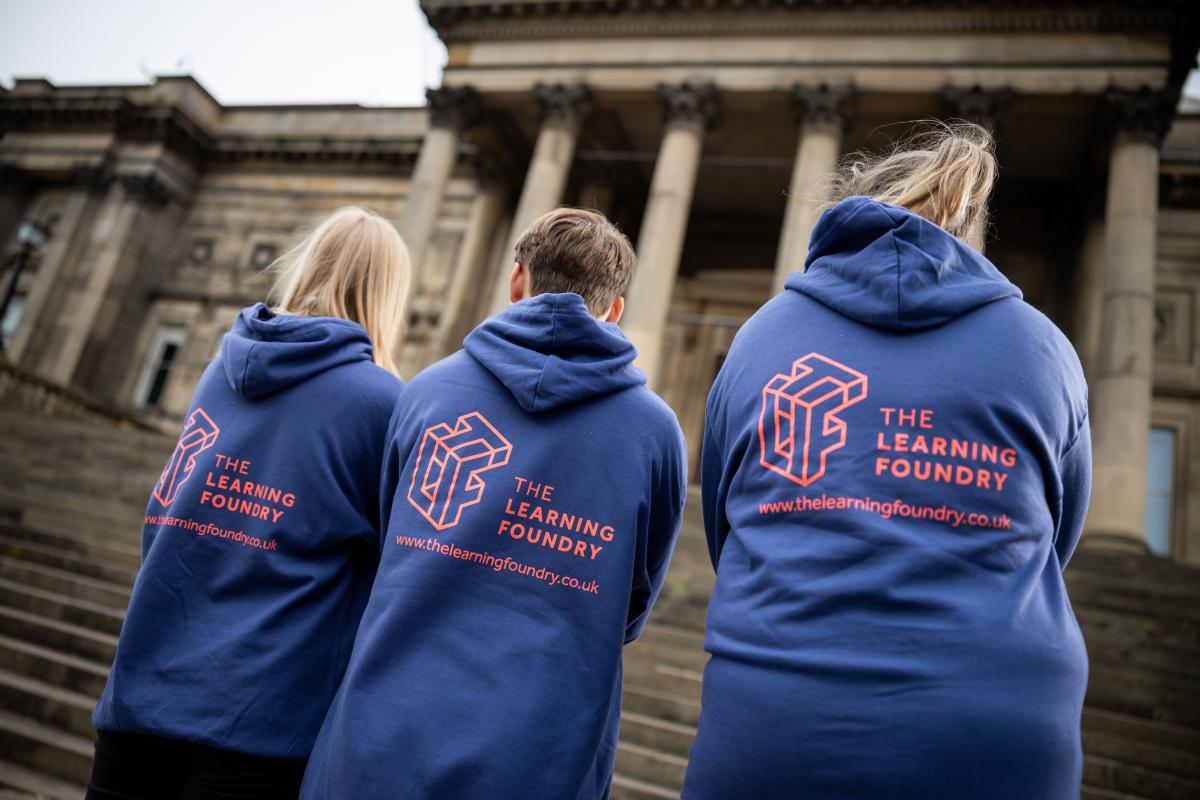 Three young people with their backs turned wearing Learning Foundry hooded tops in blue