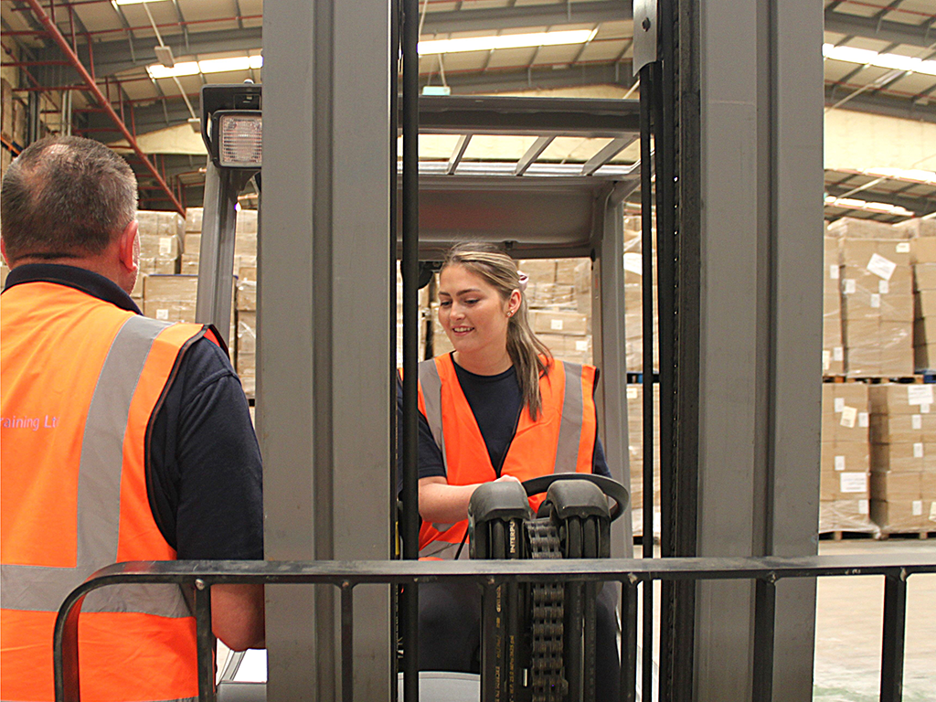 Young female using forklift truck and older male working in a warehouse