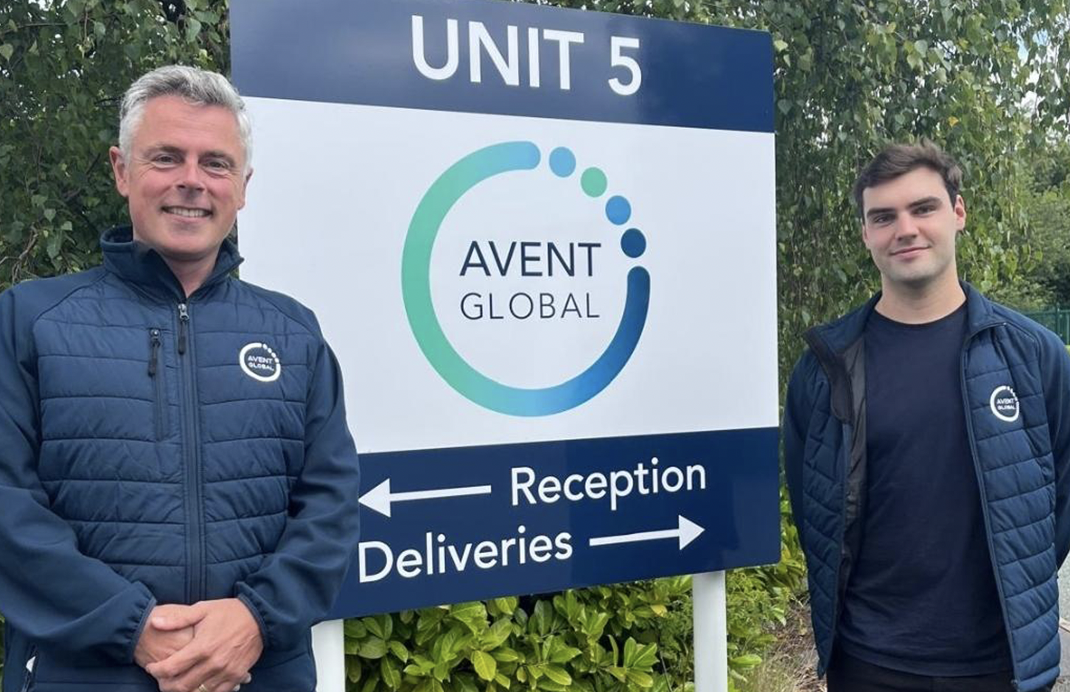 Two male members of staff by Avent Global signage